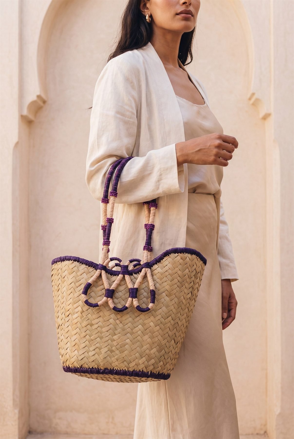 La Sculpture — panier YZA sculptural tressé main, anses violettes, porté sous une arche à Marrakech